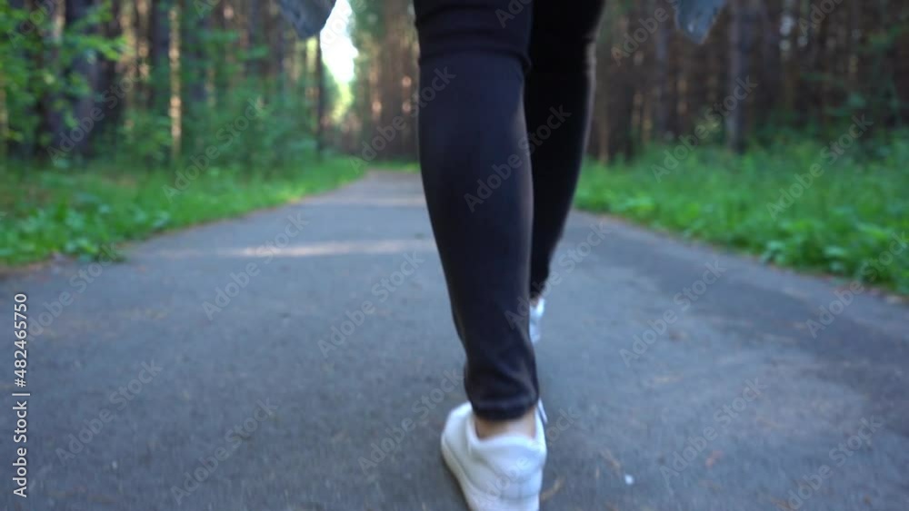 Female feet walks through the park in sneakers in summer. Slowmo. Rear view Female feet walks through the park in sneakers in summer. Slowmo. Rear view
