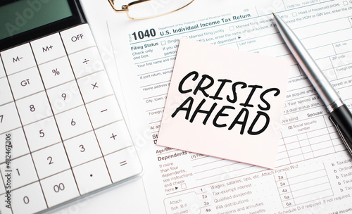 CRISIS AHEAD with pen, calculator, glass and sticker. Tax report sign