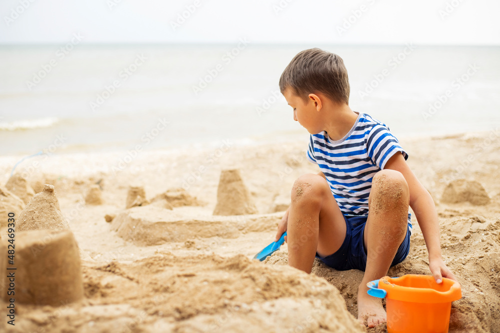 Happy child playing with sand on the beach in summer. Boy builds a sand castle on the sea Happy child playing with sand on the beach in summer. Boy builds a sand castle on the sea