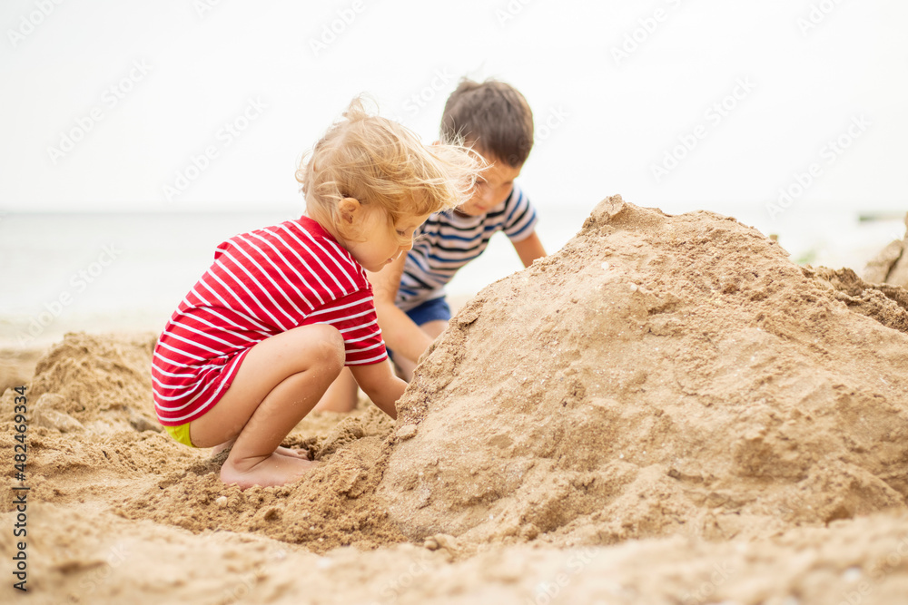 Two little boys are playing on sandy beach. Cute kids building sandcastles on beach in summer