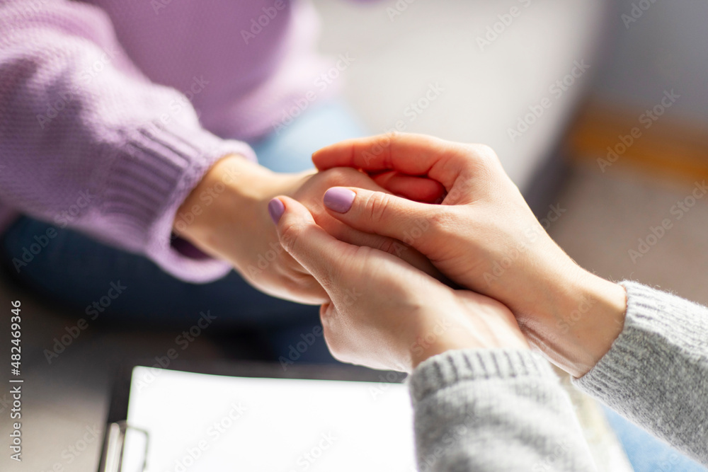 Close up of a female psychologist holding woman's hands during a therapy session. Psychotherapist supporting her depressed patient