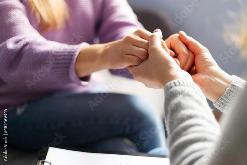 Fototapeta Naklejka Na Ścianę i Meble -  Close up of a female psychologist holding woman's hands during a therapy session. Psychotherapist supporting her depressed patient