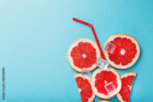Fotografia A composition of grapefruit slices and ice cubes with a straw on a blue background in the form of a refreshing drink