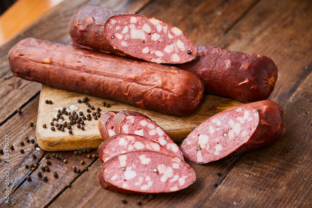 Homemade sausage with garlic cut into slices lies on a wooden table on a cutting board with spices and garlic. Traditional sausage, ready to eat, delicious breakfast. 