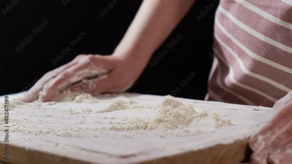 Lady in apron pours white flour on wooden board for making delicious homemade baking on black background extreme close view Lady in apron pours white flour on wooden board for making delicious homemade baking on black background extreme close view