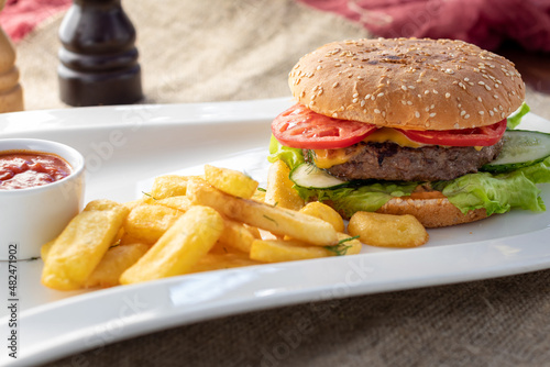 Burger with meat, tomatoes, salad and cheese on white plate with french fries