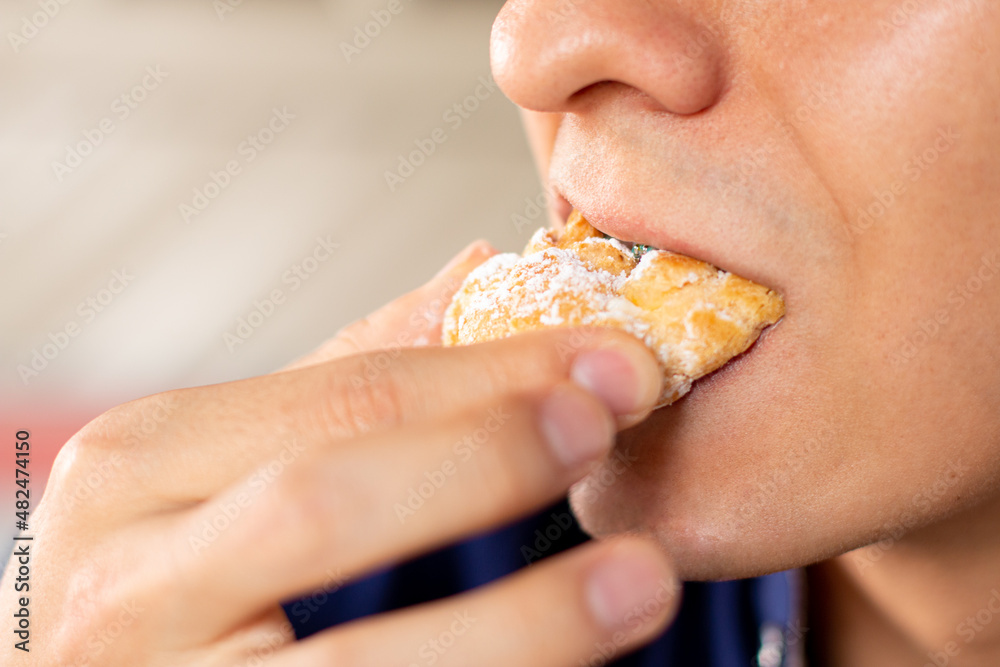 Man's mouth biting a sweet chouquette. Young adult eating a Colombian sweet bread.