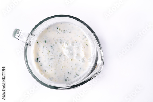 A glass of ayran with dill and parsley, highlighted on a white isolated background. Cold yogurt drink photo