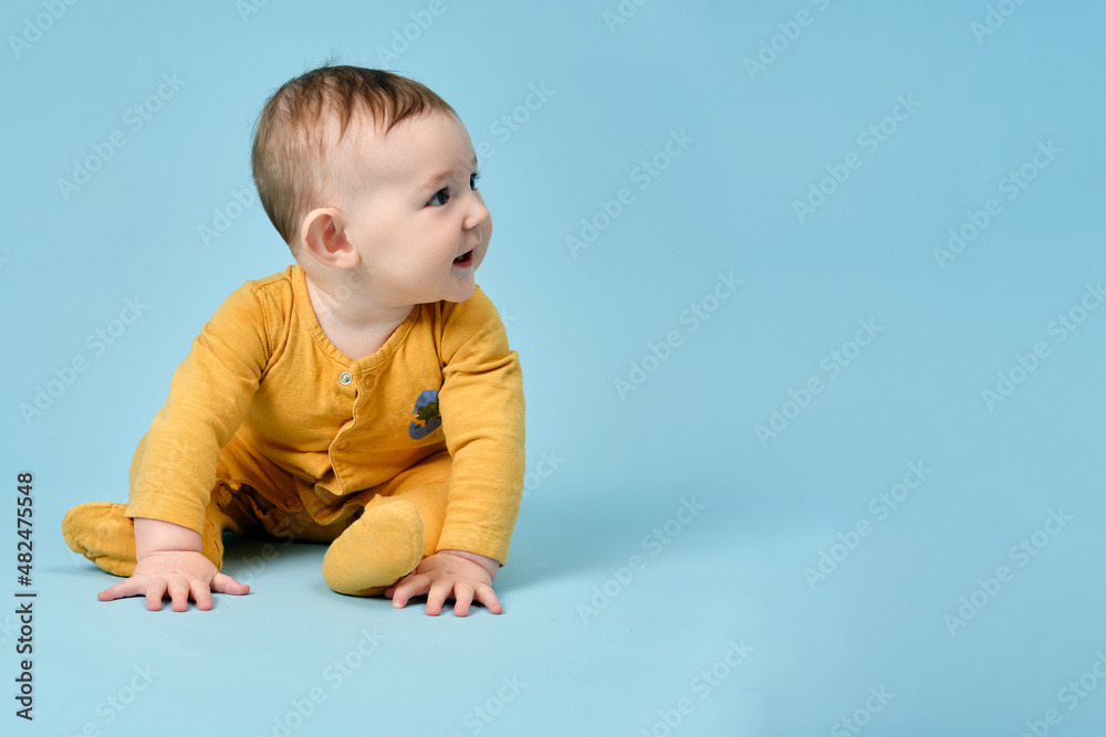 Naklejka premium Happy toddler baby sits on studio blue background. Funny child boy with a smile on his face, copy space