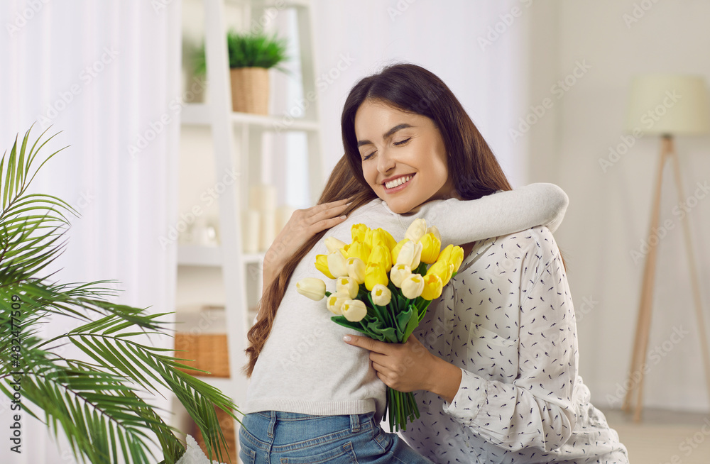 Happy young Caucasian mom hug thank loving small daughter for flowers for mothers day. Caring little girl child make surprise congratulate mum present bouquet on special occasion. Gratitude concept. Happy young Caucasian mom hug thank loving small daughter for flowers for mothers day. Caring little girl child make surprise congratulate mum present bouquet on special occasion. Gratitude concept.
