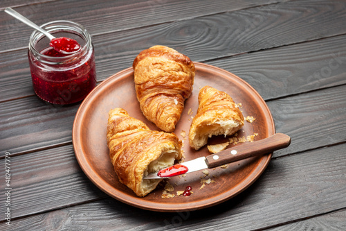 Jam on the tip of knife and croissant halfes on plate. Jar with jam. photo