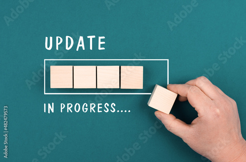 The words update in progress are standing beside the loading bar, hand puts last cube to the upload, petrol colored background © Berit Kessler