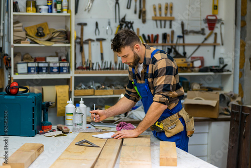 Fotografi Young handsome caucasian carpenter writing what he need for next project he need