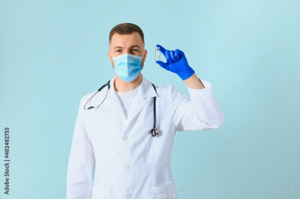 young doctor in medical mask and white coat with stethoscope holding syringe isolated on blue young doctor in medical mask and white coat with stethoscope holding syringe isolated on blue