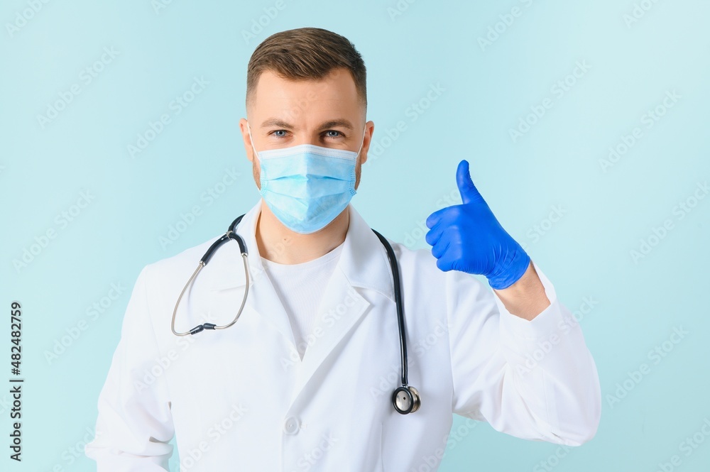 Young male doctor wearing medical mask, and stethoscope round his neck, isolated on blue background Young male doctor wearing medical mask, and stethoscope round his neck, isolated on blue background