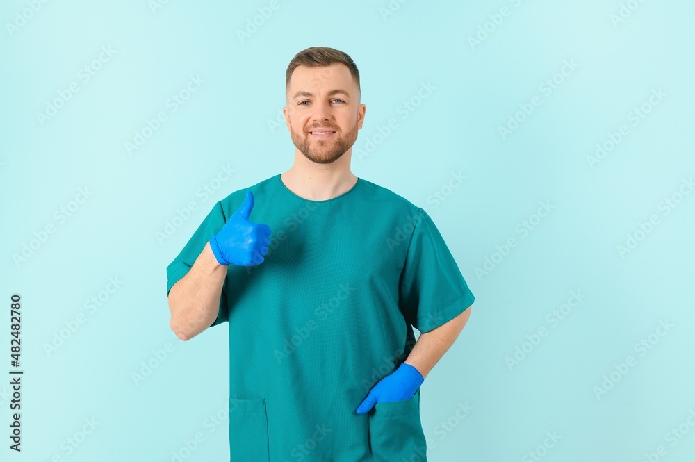 Waist up portrait view of the smiling happy doctor showing big finger at the free space on blue background. Doctor and medicine concept Waist up portrait view of the smiling happy doctor showing big finger at the free space on blue background. Doctor and medicine concept