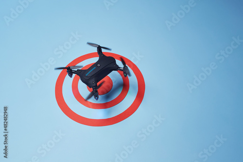 Aerial top down view on isolated drone copter with spinning propellers flying above the reached red target on the bright solid blue fond background