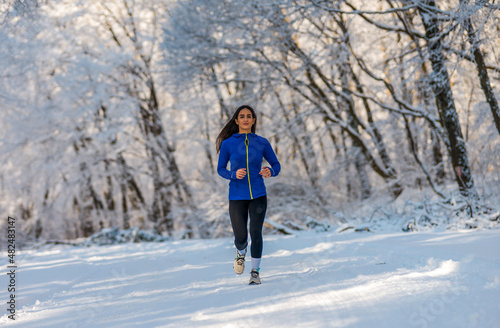 Sportswoman running in nature at snowy winter day. Winter fitness concept.