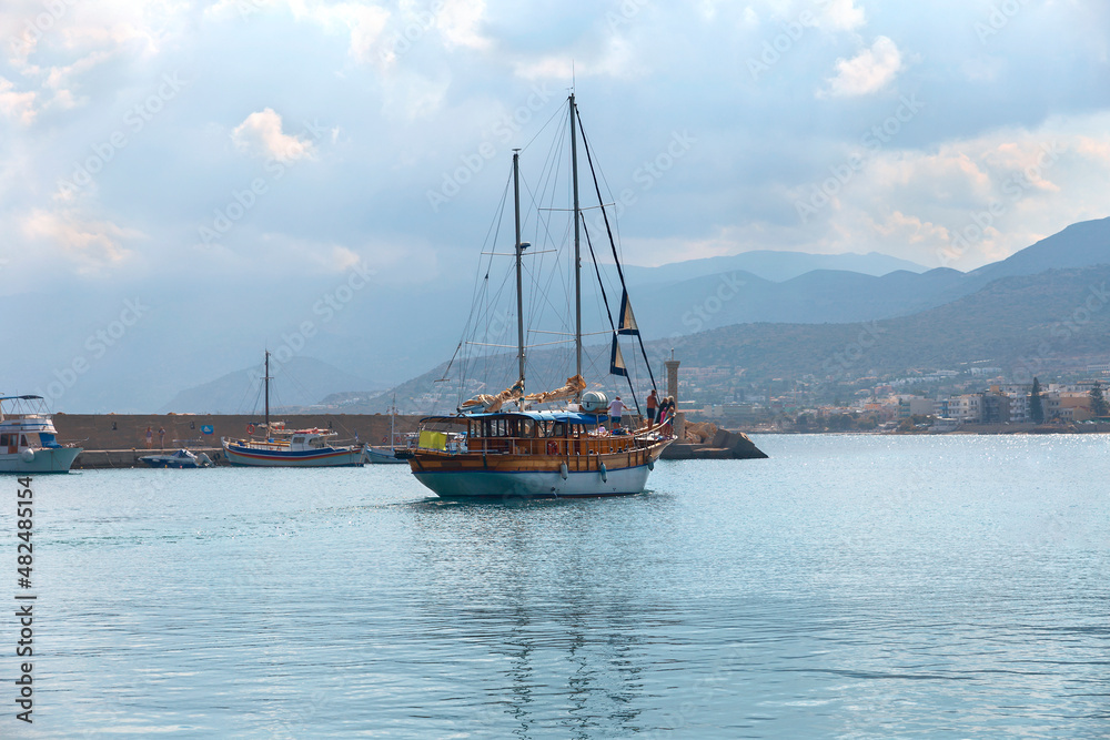 a small sailing yacht with tourists comes out of a quiet yacht into the open sea. Crete. Greece