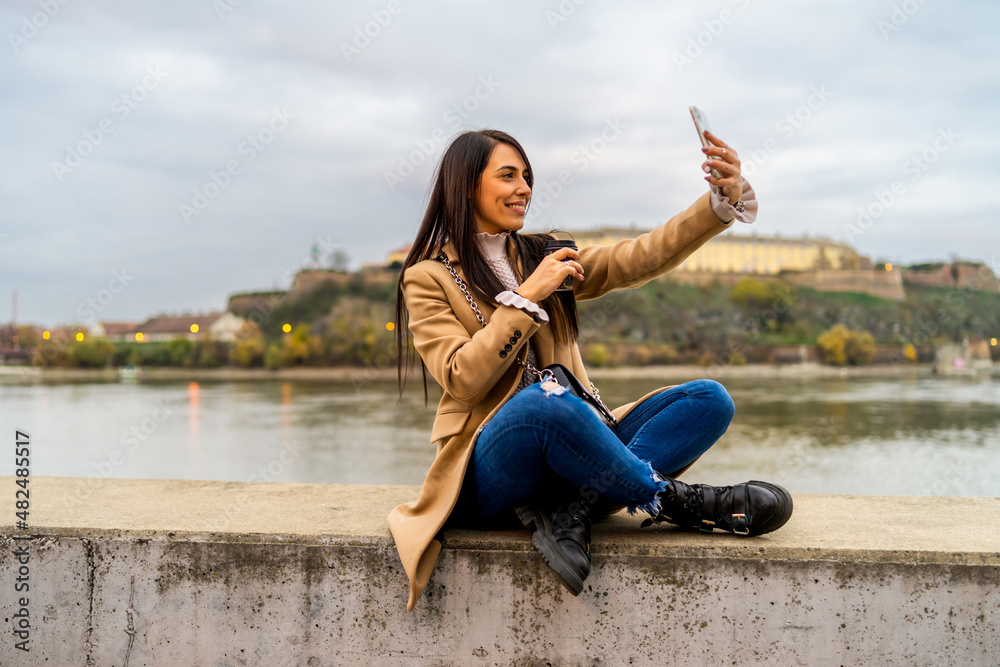 Woman taking selfie with her smartphone and drinking coffee takeaway