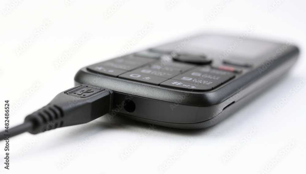 Push-button mobile phone while charging. On white background. Push-button mobile phone while charging. On white background.