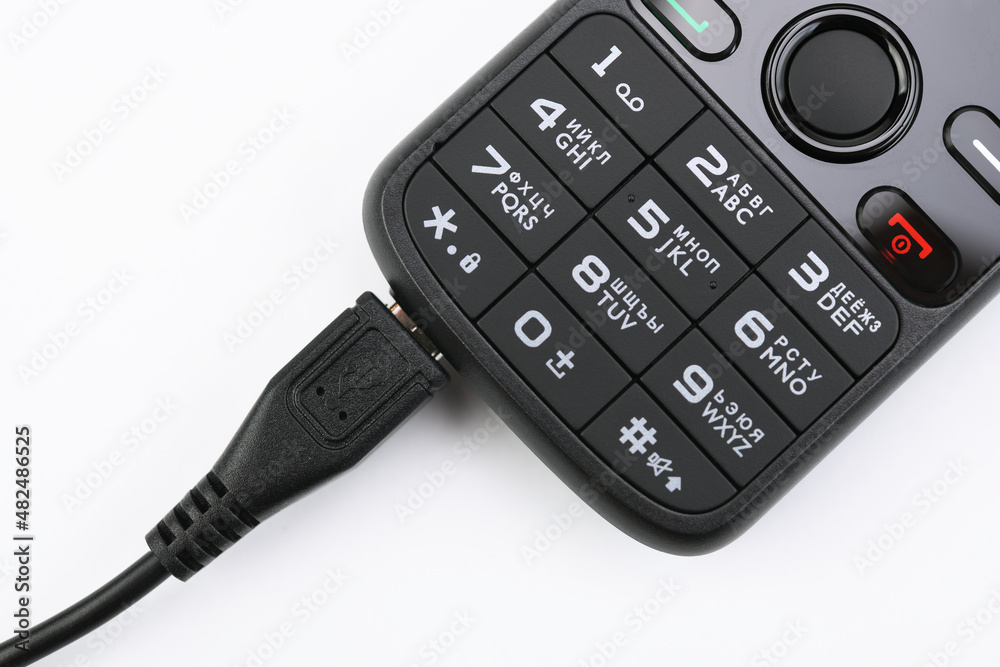Push-button mobile phone while charging. On white background. Push-button mobile phone while charging. On white background.