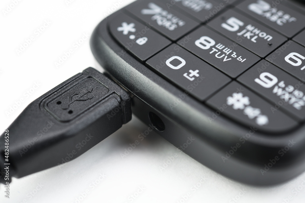 Push-button mobile phone while charging. On white background. Push-button mobile phone while charging. On white background.