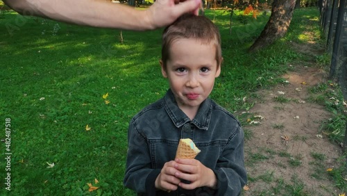 Handsome boy is eating ice cream. The father takes off the child's cap and straightens his hair.