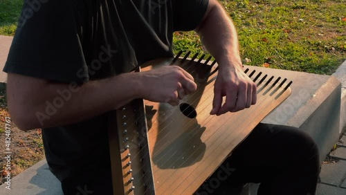 Musician hands beat the strings rhythmically. A man holds gusli on his lap and plays. Soft daylight. Close-up.