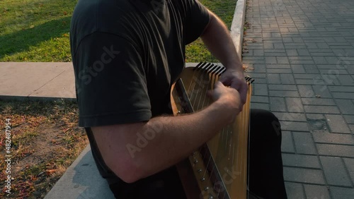 Musician hands beat the strings rhythmically. A man holds gusli on his lap and plays. Soft daylight. Close-up.