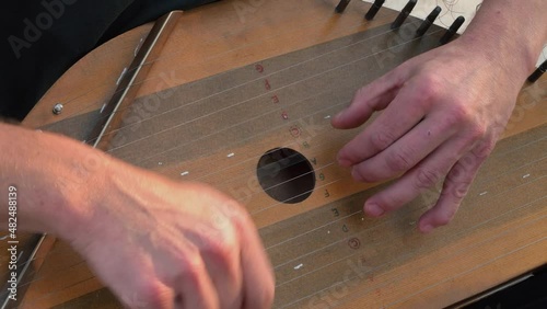 Musician hands beat the strings rhythmically. A man holds gusli on his lap and plays. Soft daylight. Close-up.