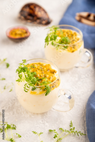Yogurt with passionfruit and marigold microgreen in glass on gray. Side view, selective focus.