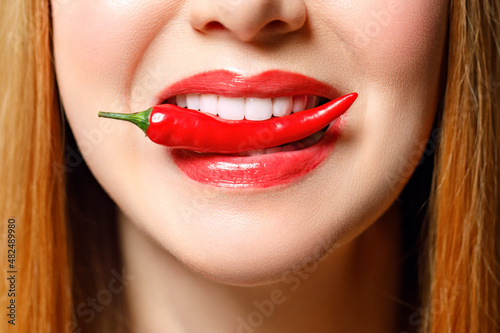 Woman with chili red pepper isolated en blue background. Sexy female lips. Hot seductive girl
