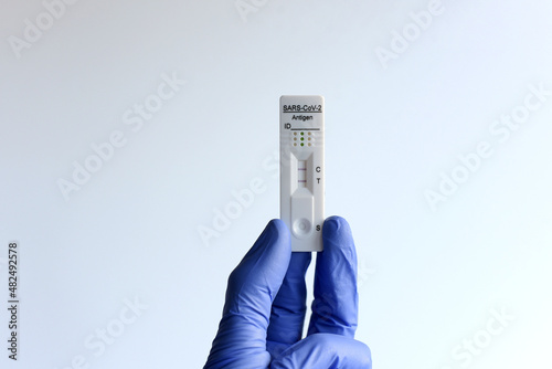 unos dedos con guantes azules sujetando un test de antigenos con resultado positivo sobre fondo blanco. covid-19
