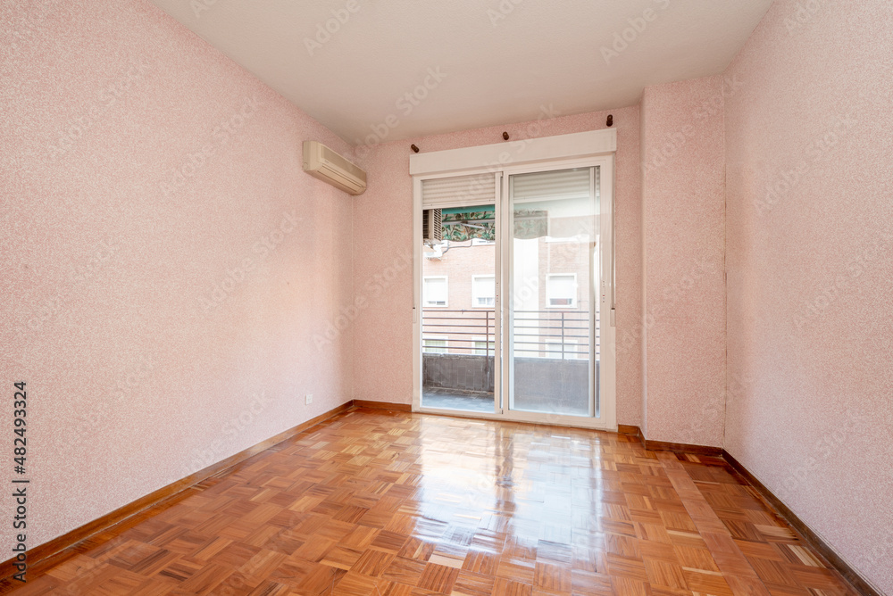 Living room with pink painted walls, reddish wooden floors and large window with white sliding doors leading out to a terrace