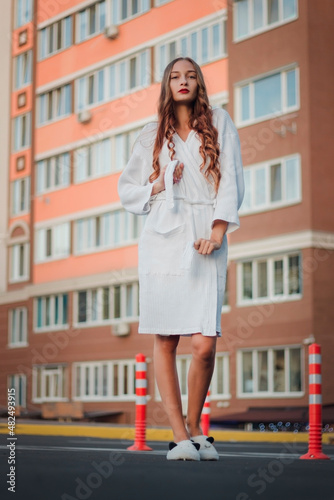 Free Download Full length cute pretty woman in white bathrobe outdoors. Curly hair. Red lips. Outdoor morning street portrait. Concept - GFXLoad