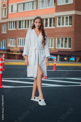 Full length cute pretty woman in white bathrobe outdoors. Curly hair. Red lips. Outdoor morning street portrait. Concept