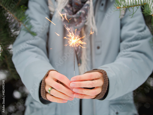 Woman celebrates Christmas or New Year with bright sparkler. Bengal fire, traditional firework for winter holiday celebration outdoors.