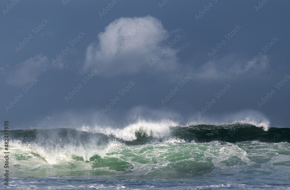 Naklejka premium Seascape. Powerful ocean wave on the surface of the ocean. Wave breaks on a shallow bank. Stormy weather, stormy clouds sky background.
