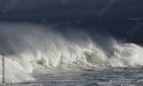 Seascape. Powerful ocean wave on the surface of the ocean. Wave breaks on a shallow bank. Stormy weather, stormy clouds sky background.