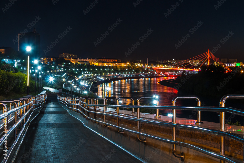Obraz premium Beautiful view of the illuminated Embankment of Tura River and the Bridge of Lovers at dusk, Tyumen, Russia 