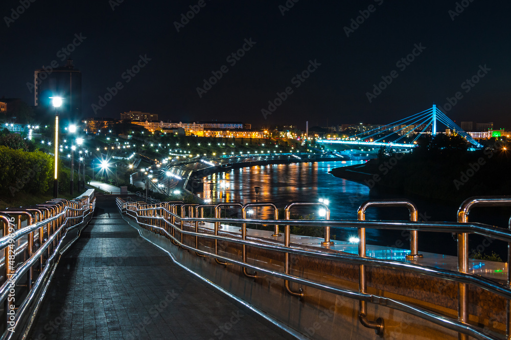 Obraz premium Beautiful view of the illuminated Embankment of Tura River and the Bridge of Lovers at dusk, Tyumen, Russia 