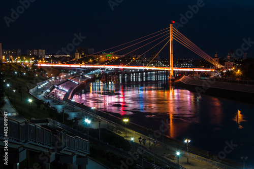 Beautiful view of the illuminated Embankment of Tura River and the Bridge of Lovers at dusk, Tyumen, Russia 