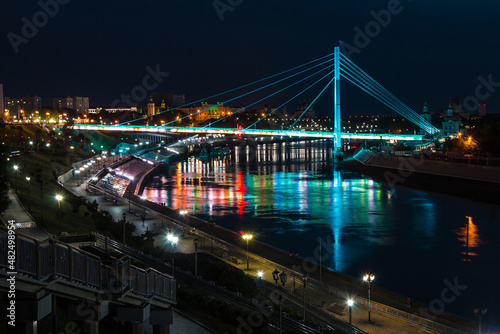 Beautiful view of the illuminated Embankment of Tura River and the Bridge of Lovers at dusk, Tyumen, Russia 