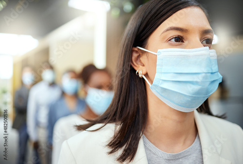 The safe way to work. Cropped shot of an attractive young businesswoman wearing a mask while standing at the head of a queue in her office.