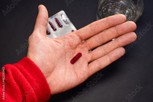Person taking medication with black background with blister and water.