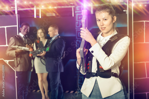 Woman in business suit holding a laser gun and playing laser tag with colleagues