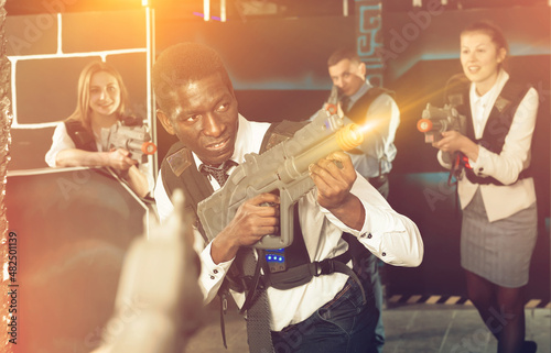 Cheery Afro man and his colleagues having corporative entertainment in laser tag room