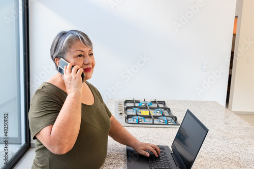 Senior woman 68 years old working on laptop and watching video in kitchen
