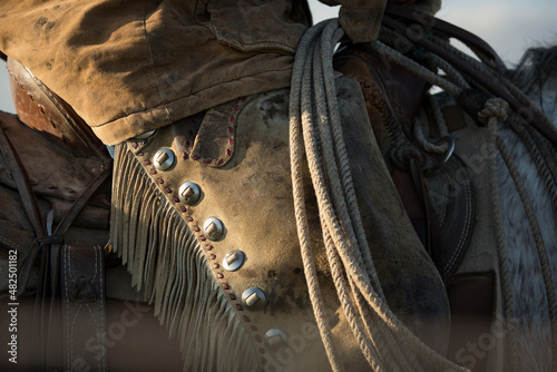 Fotografía Cowboy on horseback wearing chaps with his lasso or rope resting on the horn of